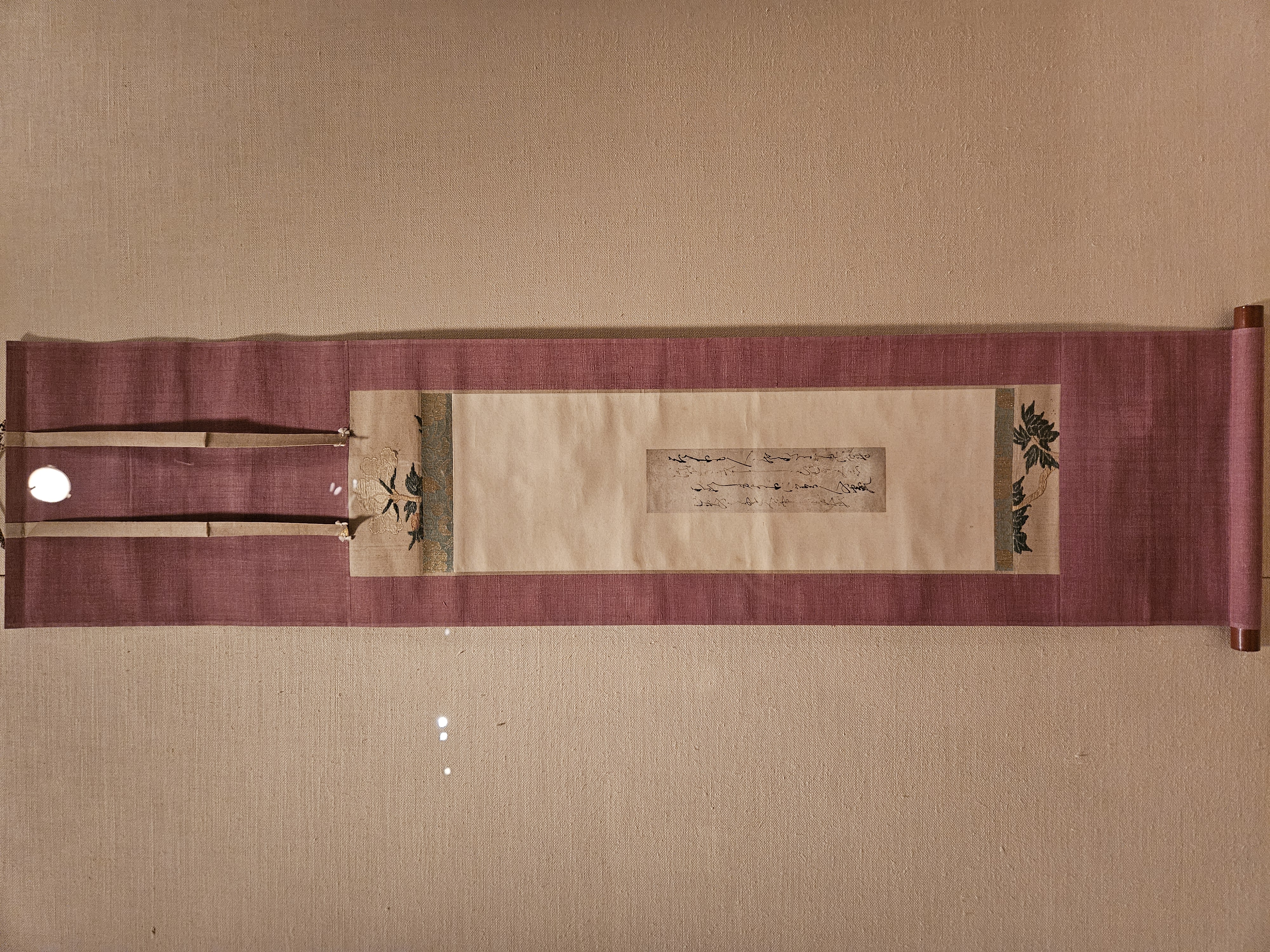 A calligraphic poem mounted on embrodered paper, on a long maroon scroll.